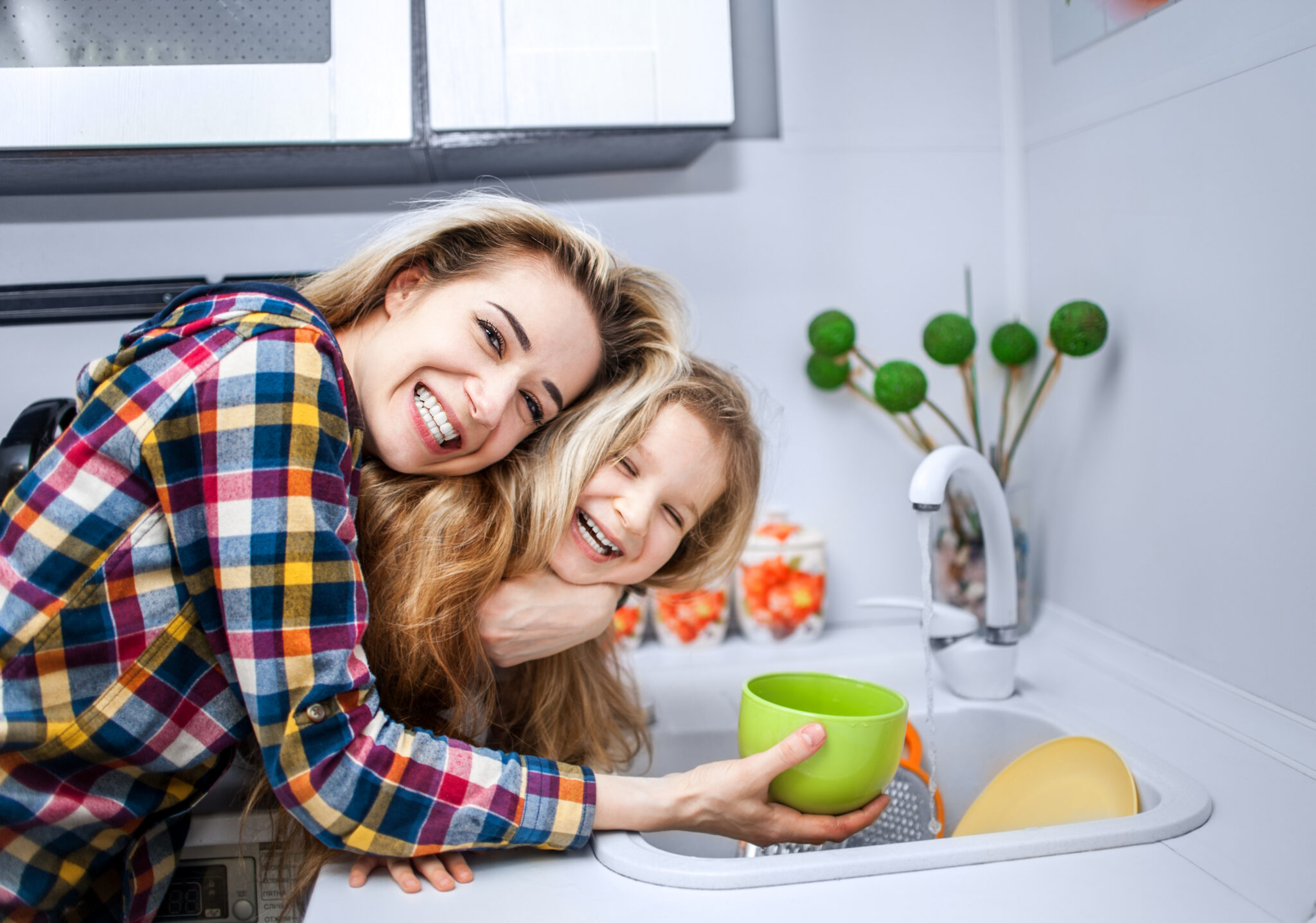 A smiling au pair hugging a laughing young girl in a kitchen