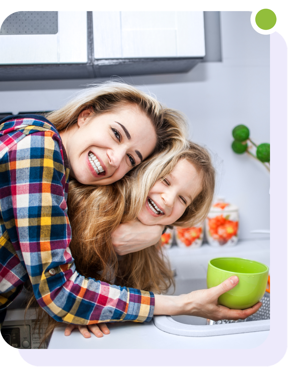 A mother hugs her laughing daughter at the kitchen sink