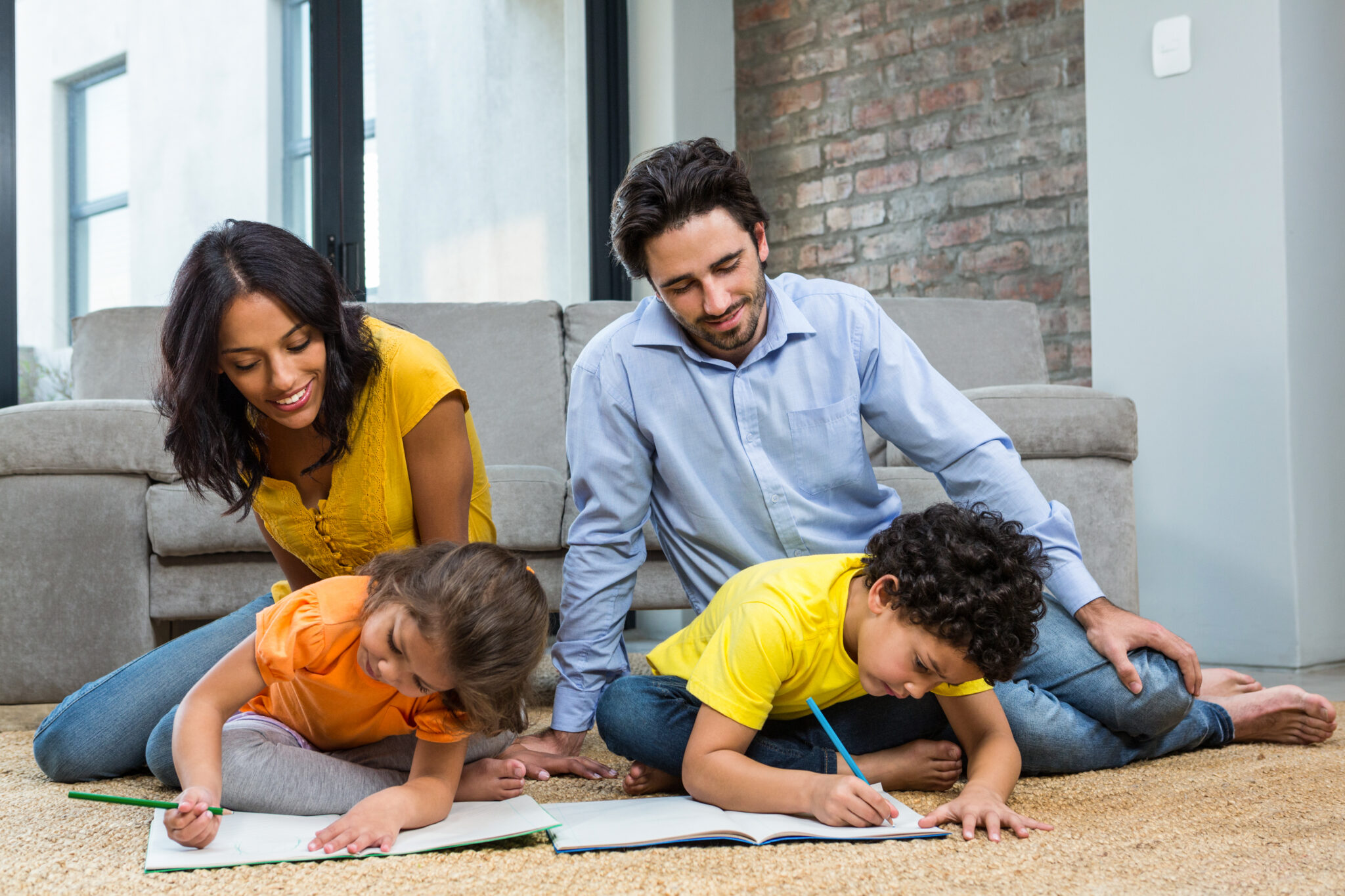 A mother and father sitting on the floor with their two children, who are drawing