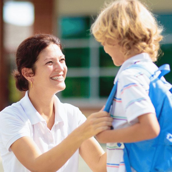 An au pair smiling at a young boy with a school backpack