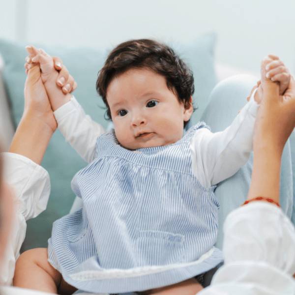 An infant care au pair holding a baby’s hands during play