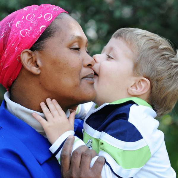 A nanny being kissed on the cheek by a young child in her care