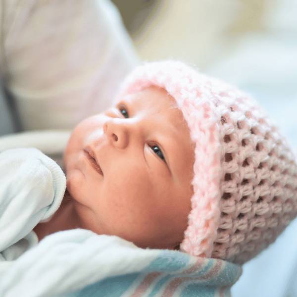 A newborn baby in a pink knitted hat being held close